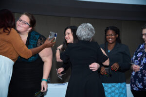 ElderSource CEO Linda Levin hugging a member of the Veteran-Directed Care team while four women hold their awards.