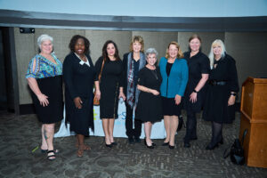 Seven women stand in a line posing for a photo with ElderSource's CEO.